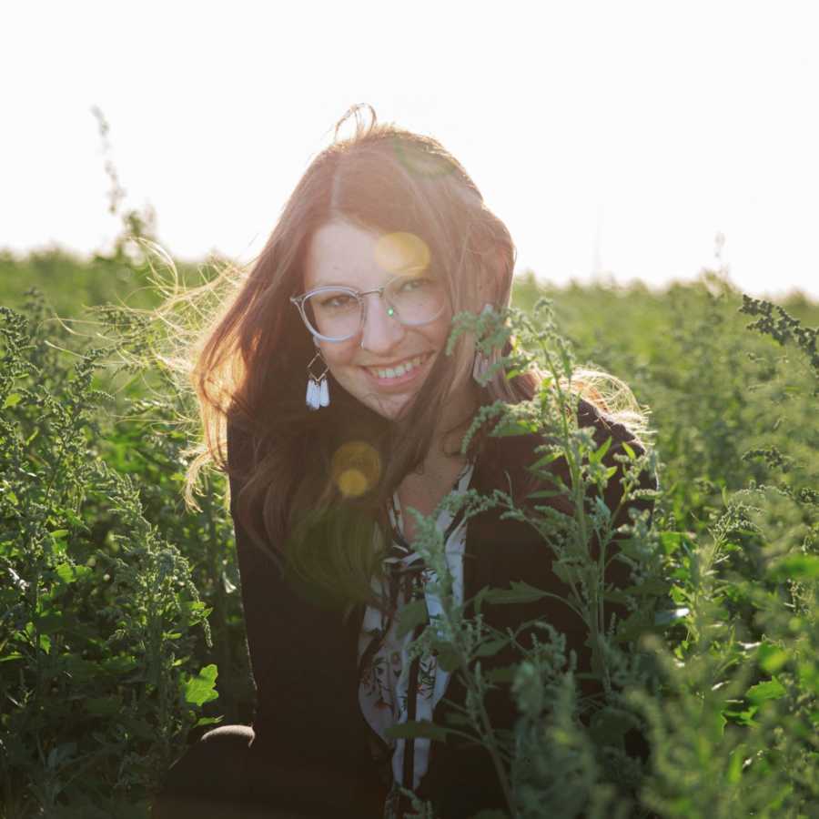 Woman with glasses on takes photo out in a field during a photoshoot