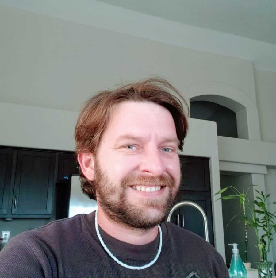 Man with full beard and a chain on smiles as he takes a selfie