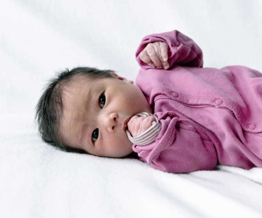 An infant girl in a pink onesie looks in the camera for a newborn photo