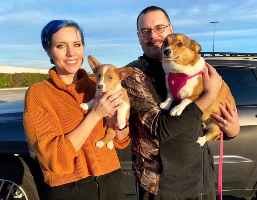 couple holding two corgis