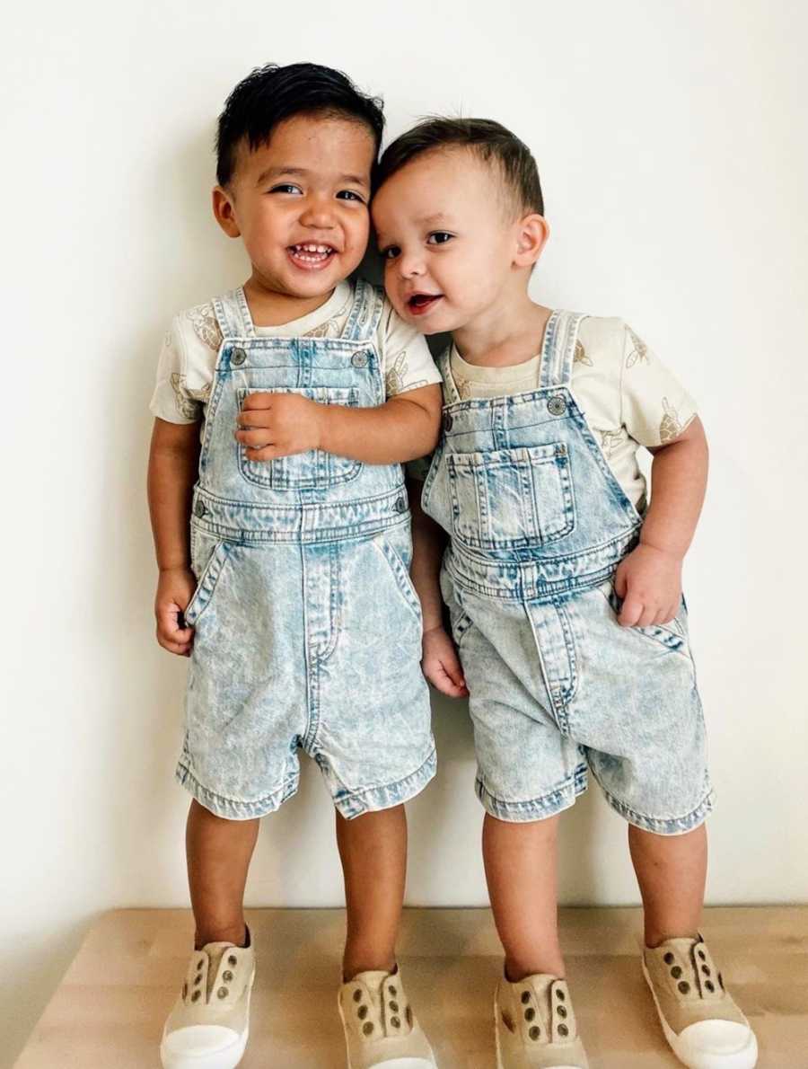 Brothers standing in front of white wall wearing overalls