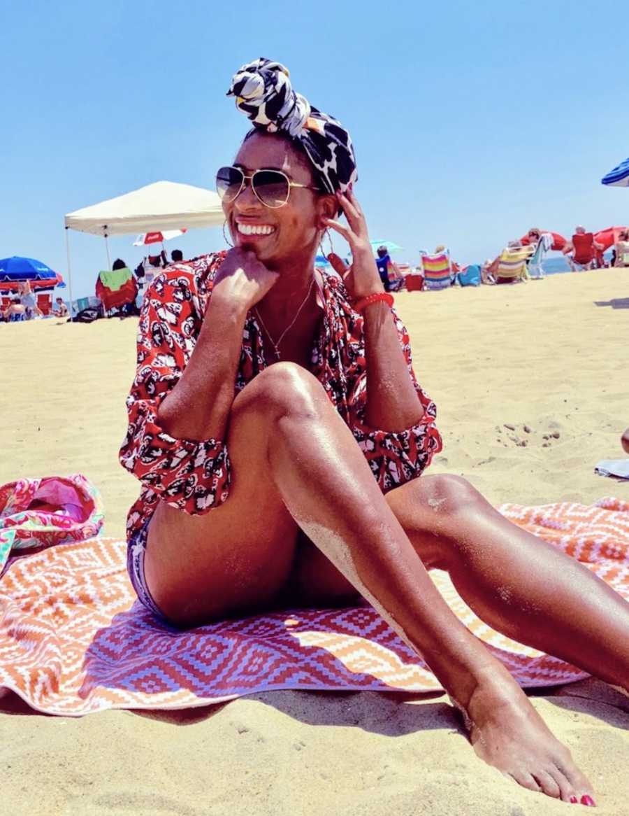 Woman smiling wearing sunglasses sitting on towel at the beach