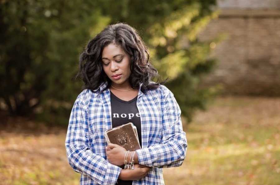 Woman standing by pine tree looking down holding a Bible