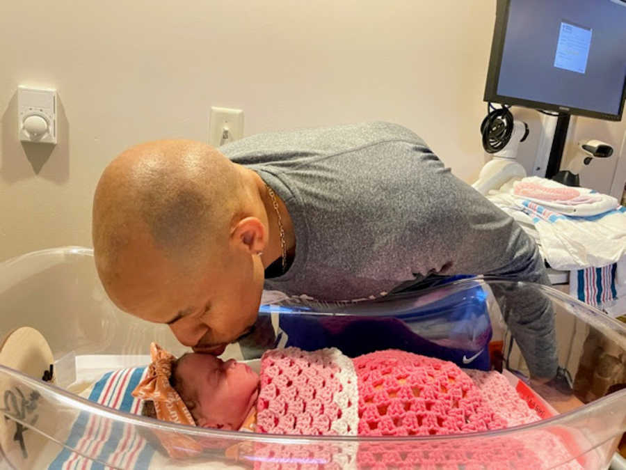 Man leaning down to kiss newborn daughter wrapped in pink blanket