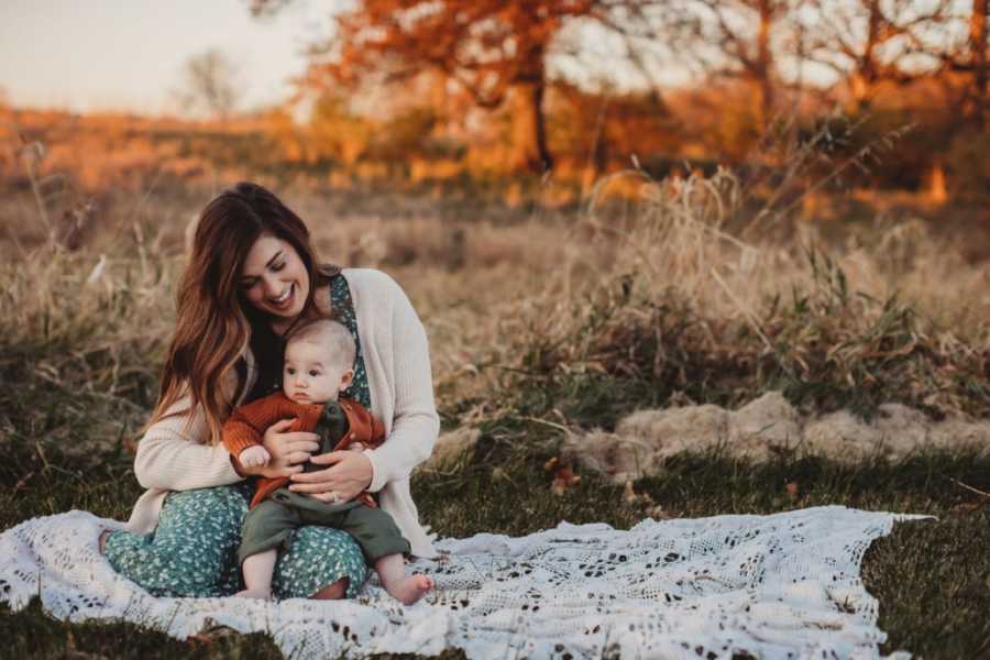 Woman smiles down at her baby boy during an outside photoshoot at sunset