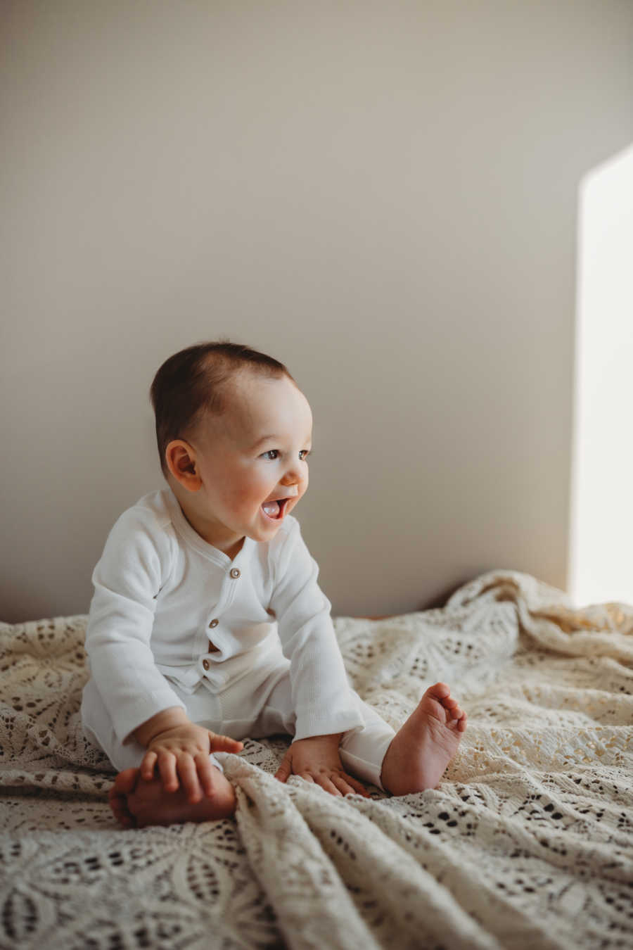 18-month baby gives a toothless smile in a white onesie