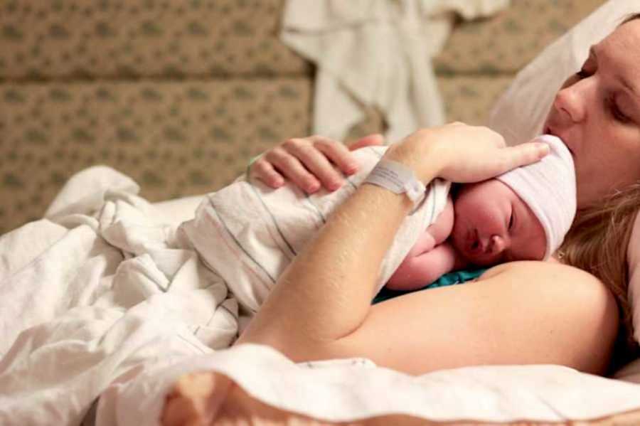 Woman lying on bed with newborn on top of her