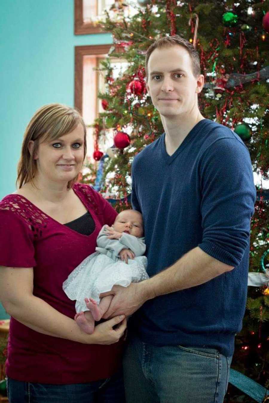 couple holding baby in front of Christmas tree