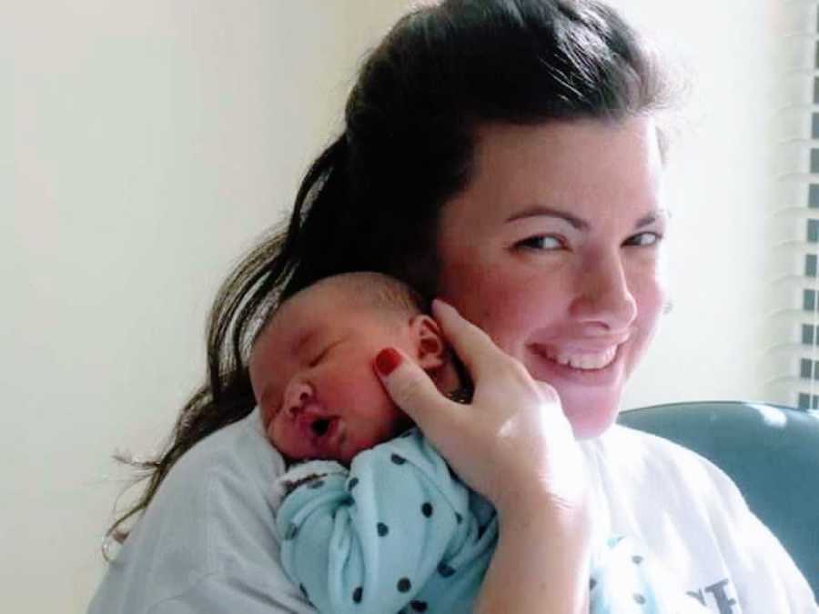 Woman holds her newborn baby while she naps in the hospital after birth