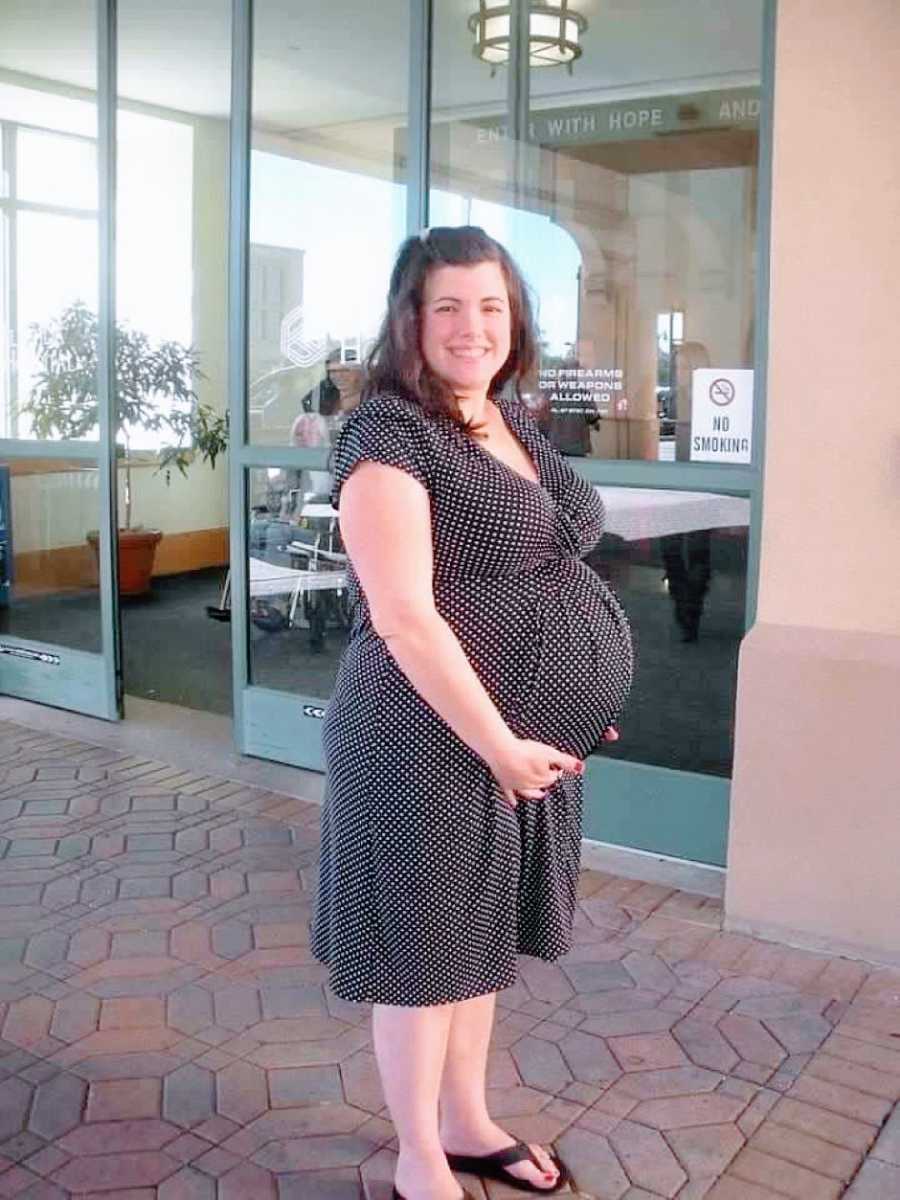 Woman pregnant with her first daughter holds her belly and smiles outside of the hospital