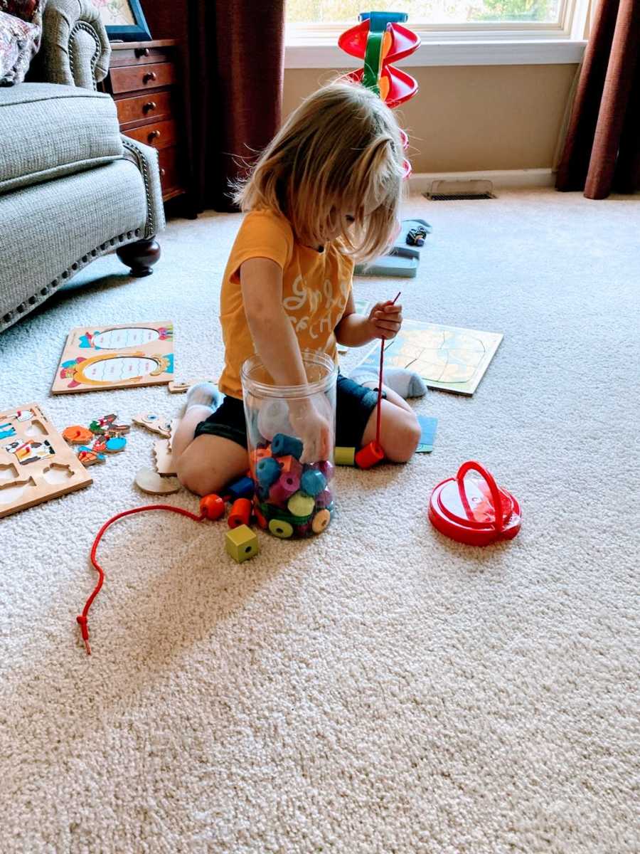 Young toddler concentrates on building a toy out of building blocks while being babysat