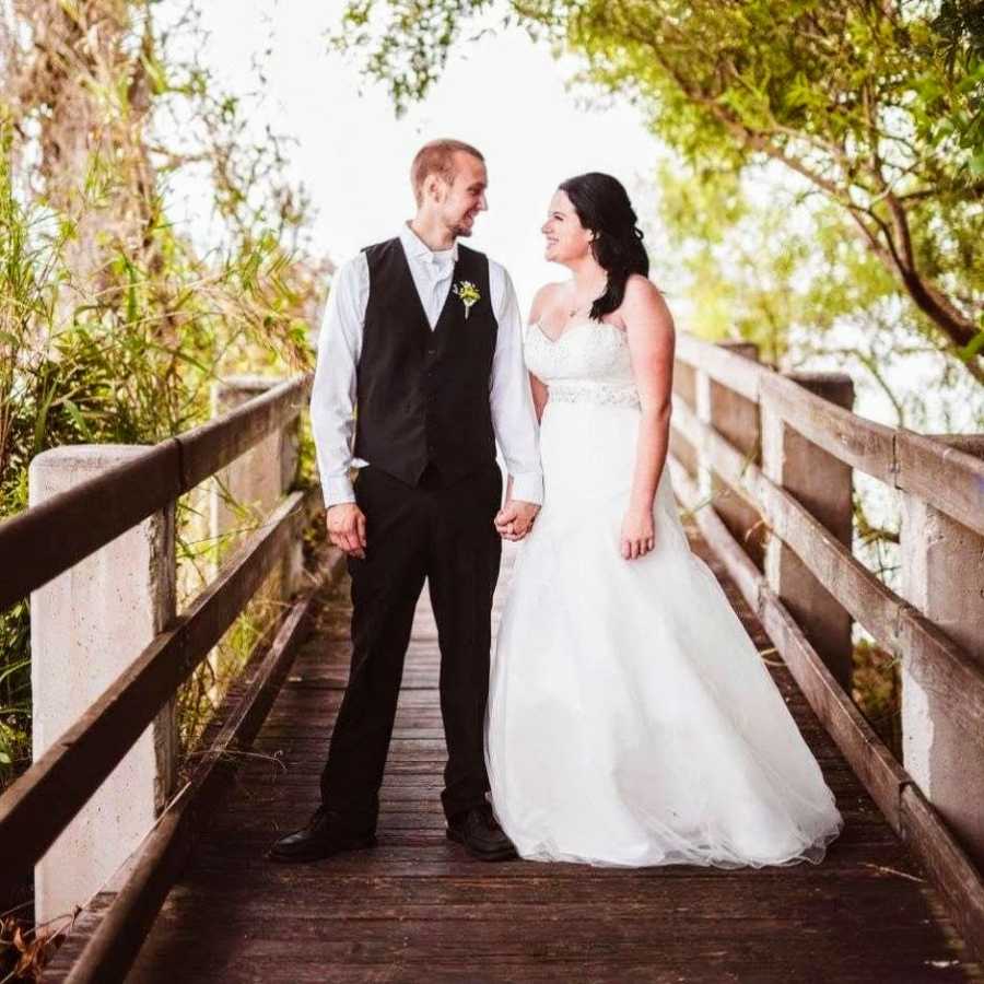 Newly married couple pose for an outdoor photo on a bridge while smiling at each other