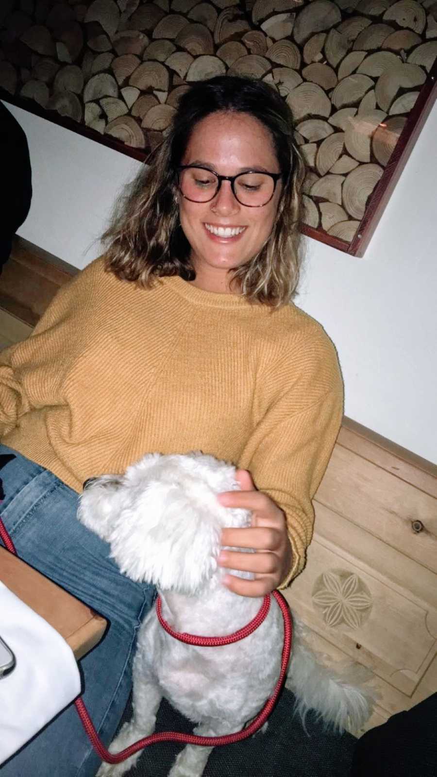 Woman in yellow sweater smiles down at a white dog while petting it