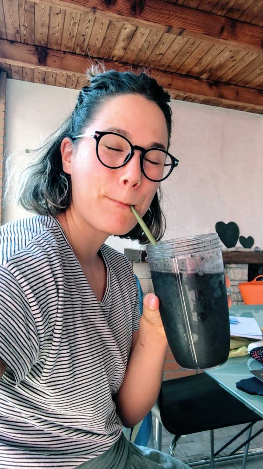 Woman in glasses smiles and enjoys a dark smoothie