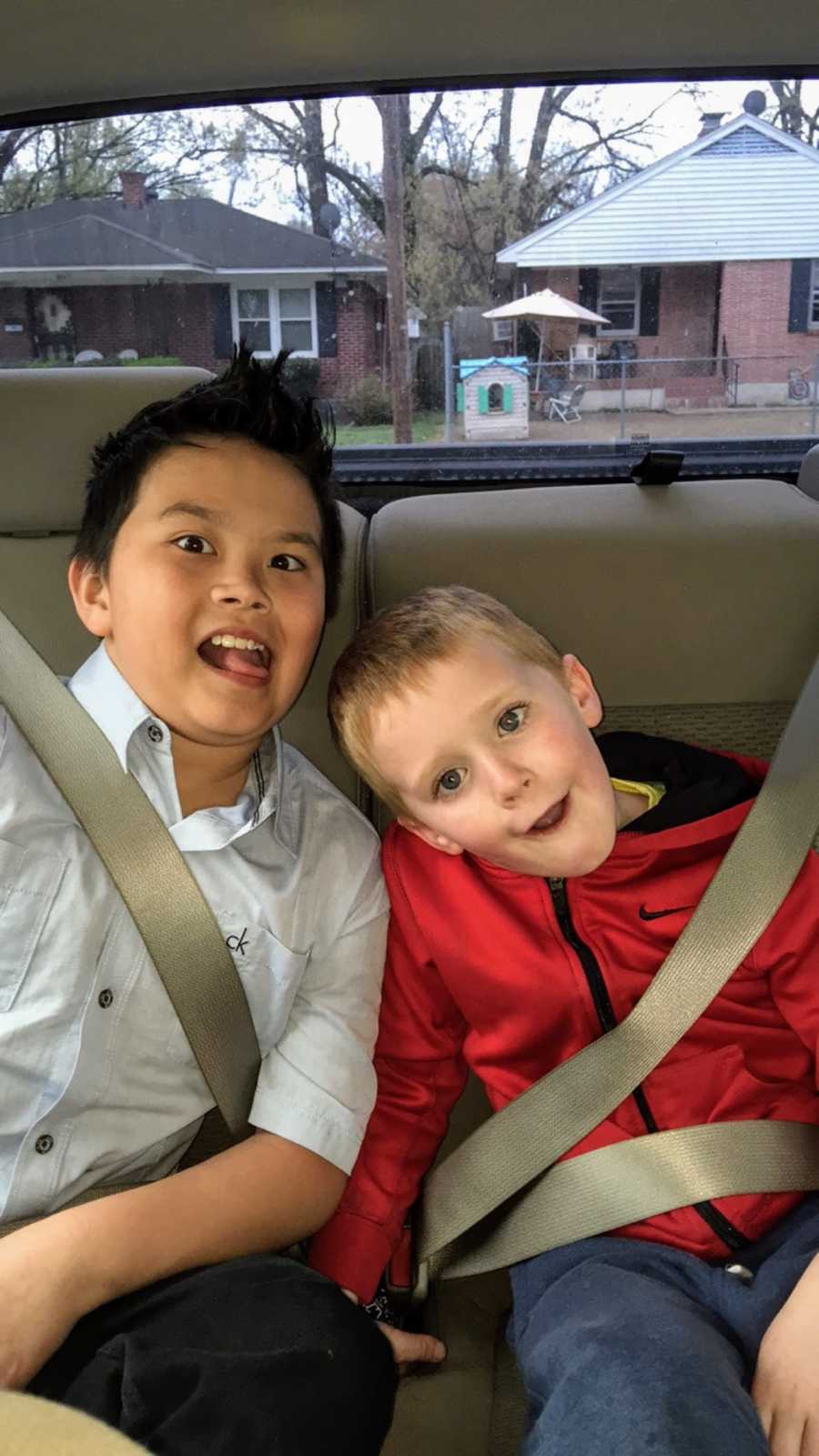 A pair of young brothers sit in the back of their mom's car