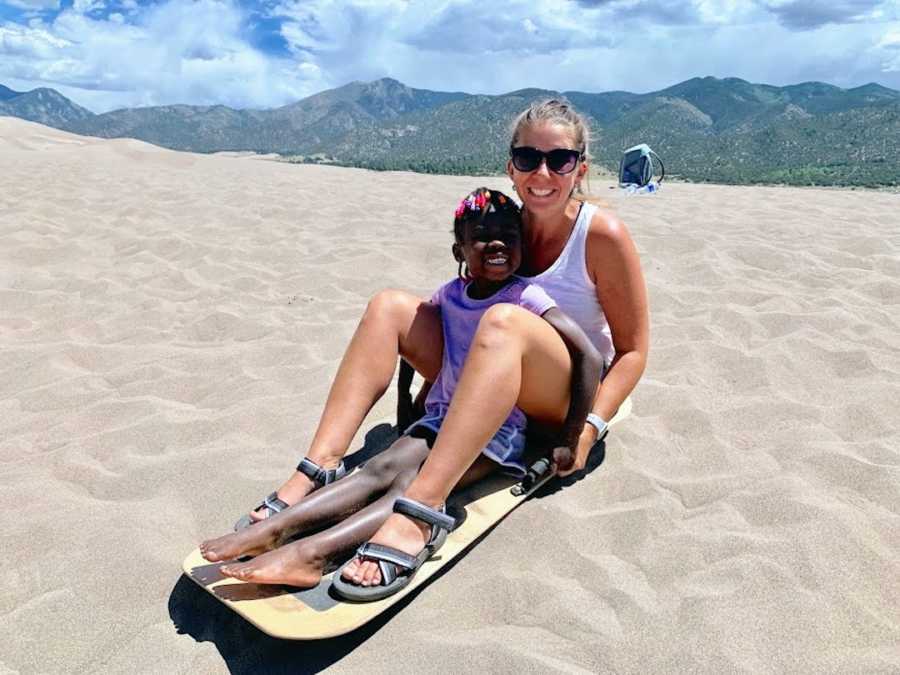 Mother and daughter sitting on sled in sand