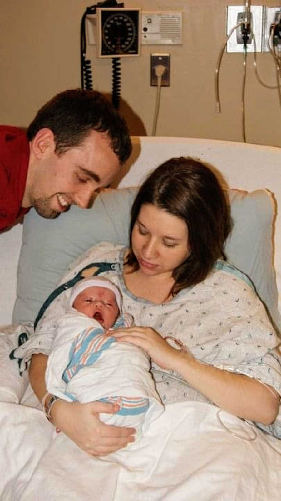 New father and new mother holding newborn baby in hospital bed