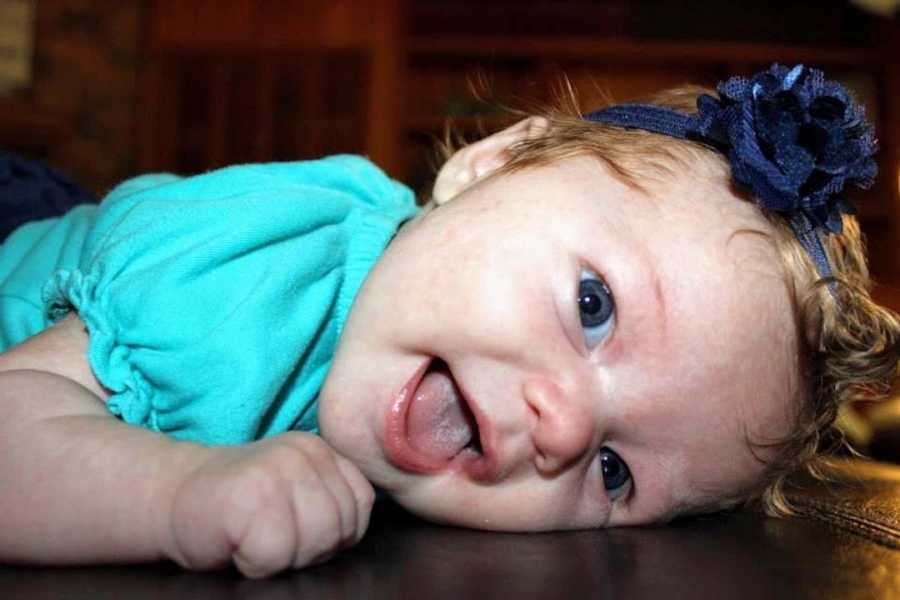 Baby girl wearing blue shirt lying on floor 