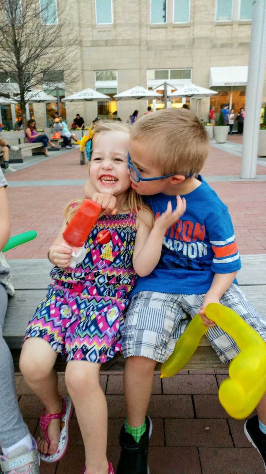 Sister and brother sitting outside with brother kissing sister on the cheek