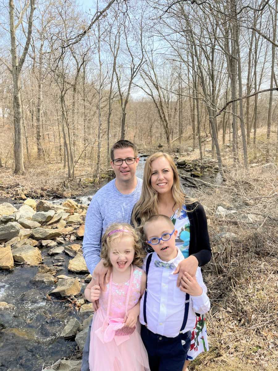 Family of four standing in the woods smiling