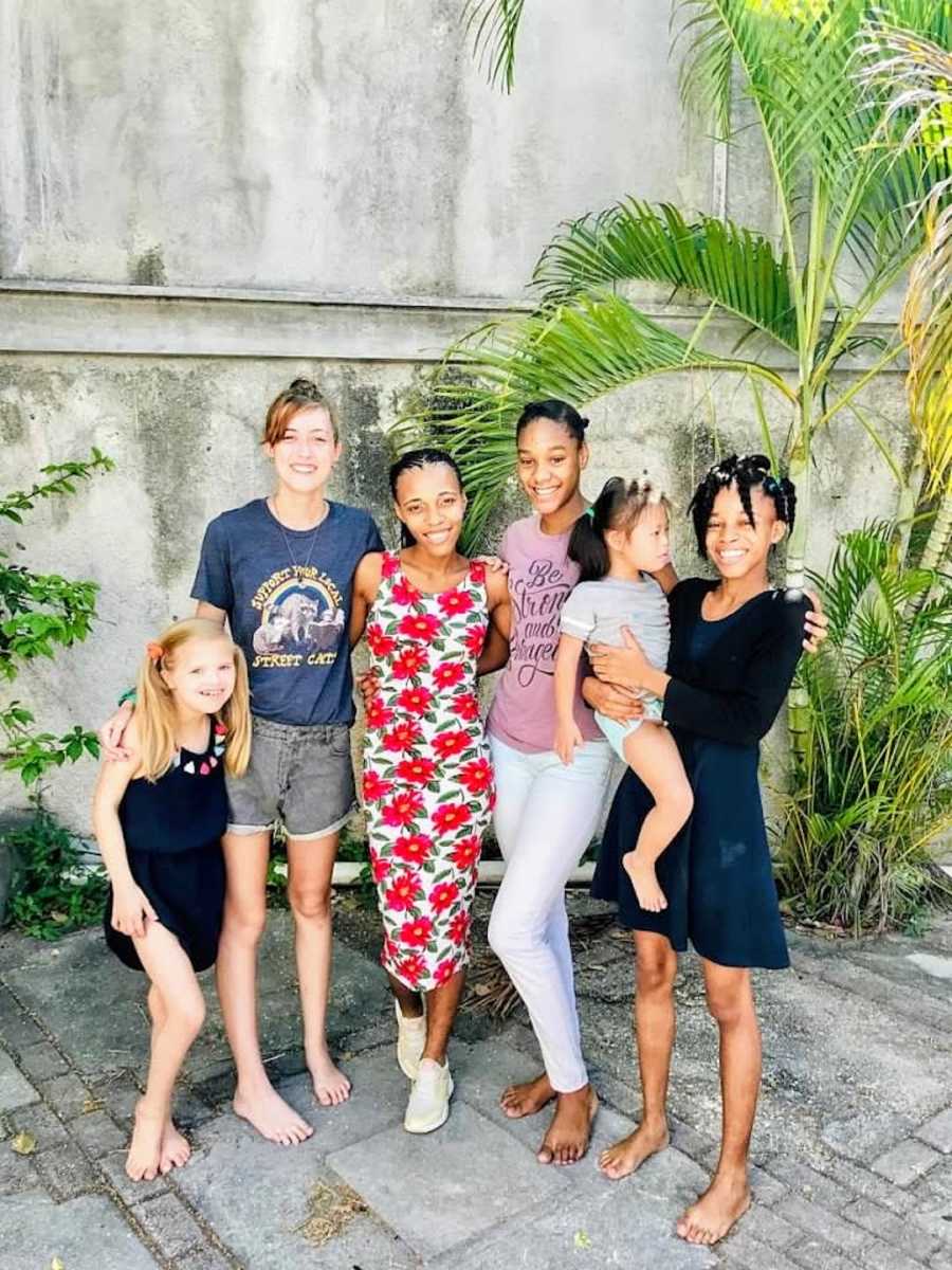 Six female siblings standing outside with palm trees smiling