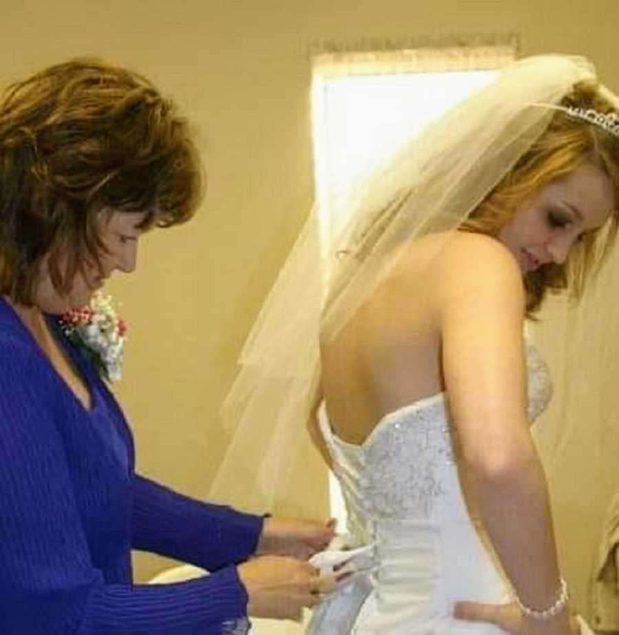 A mother zips up her daughter's wedding dress
