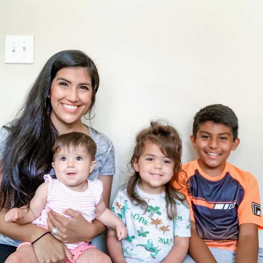 Mother sitting in front of white wall with three children and smiling