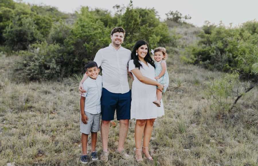 Family of four standing in nature smiling wearing white