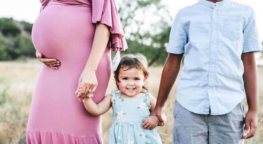 Pregnant woman wearing pink with two children holding hands and smiling