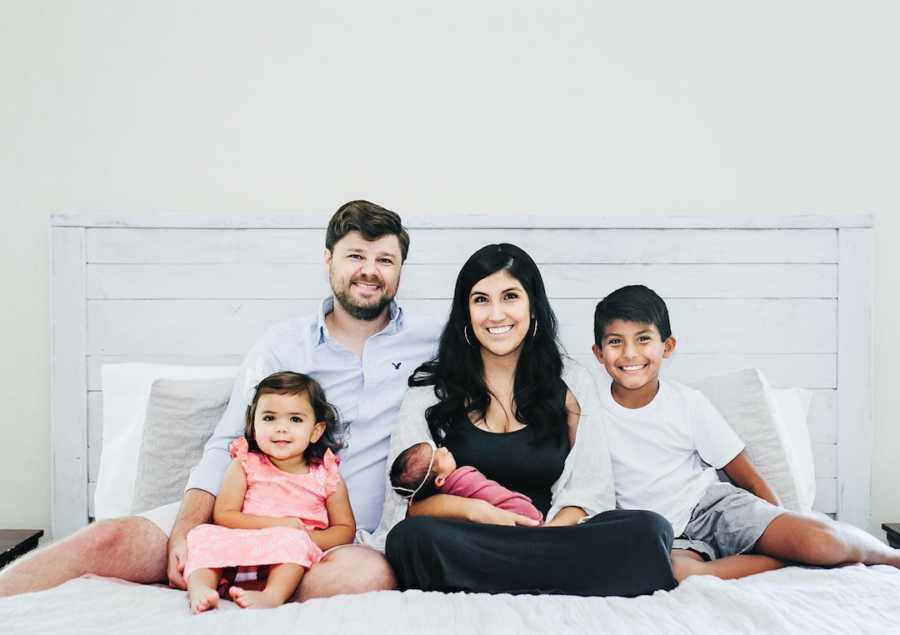 Family of five sitting on white bed and smiling