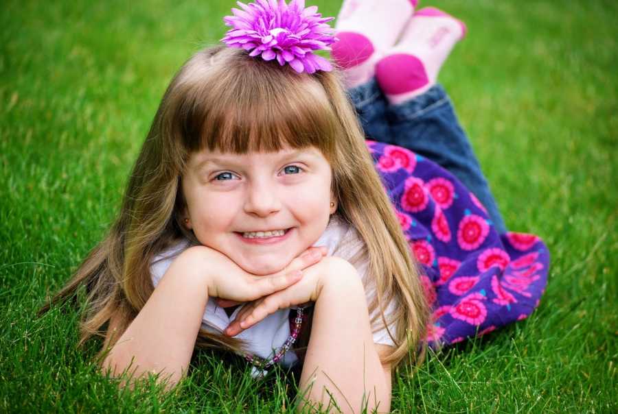 An adopted girl lies on her stomach in the grass wearing pink