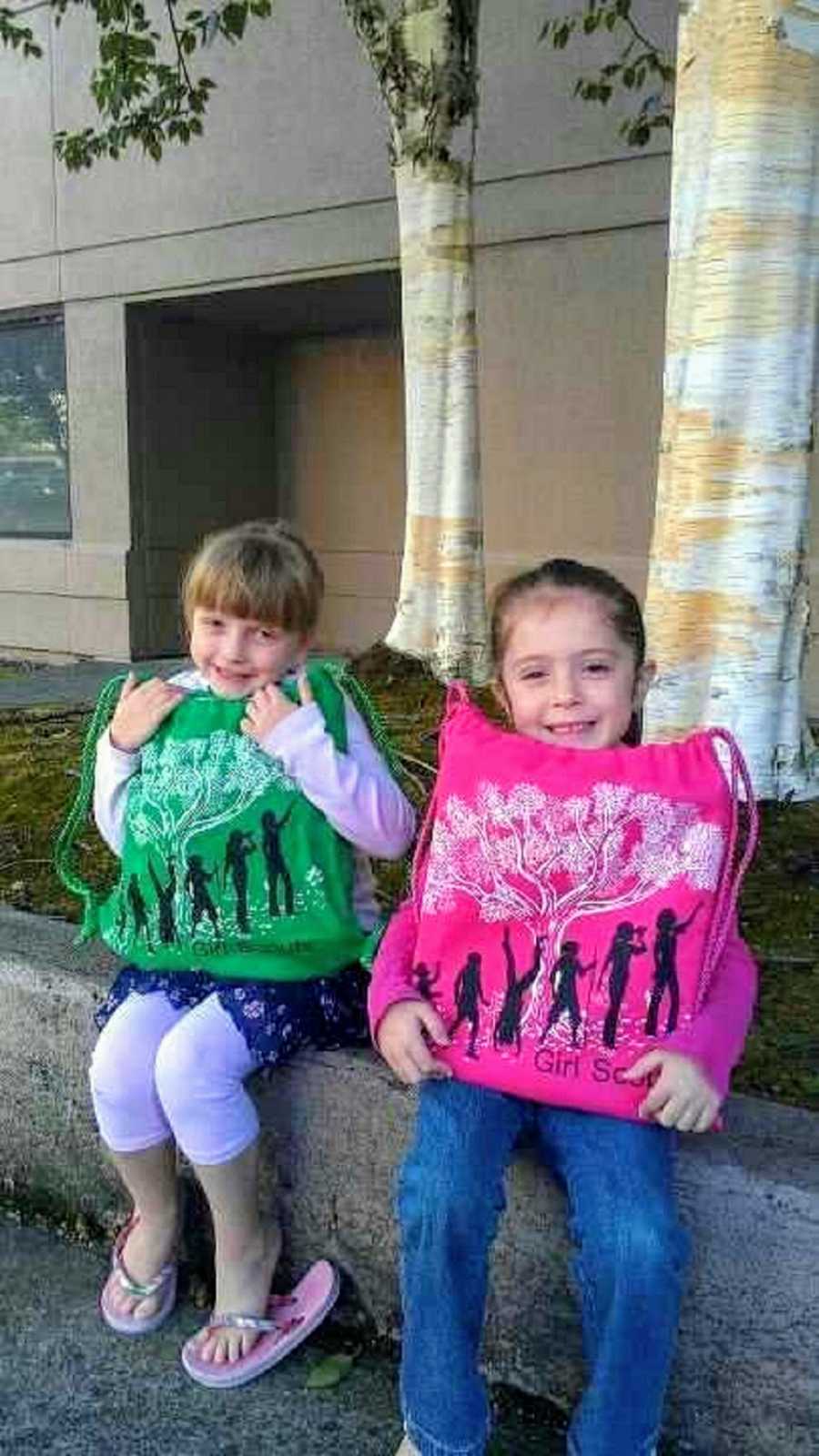 Adoptive sisters hold up pink and green bags