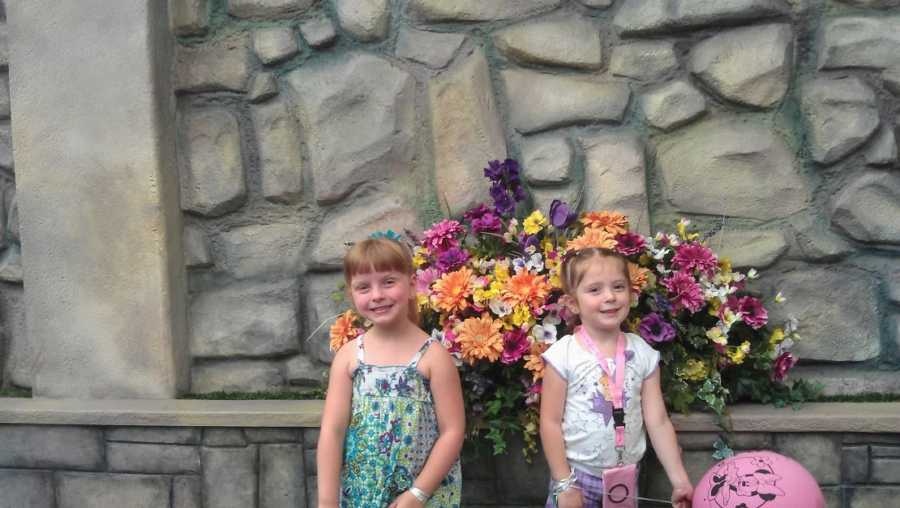 Two adoptive sisters stand in front of flowers