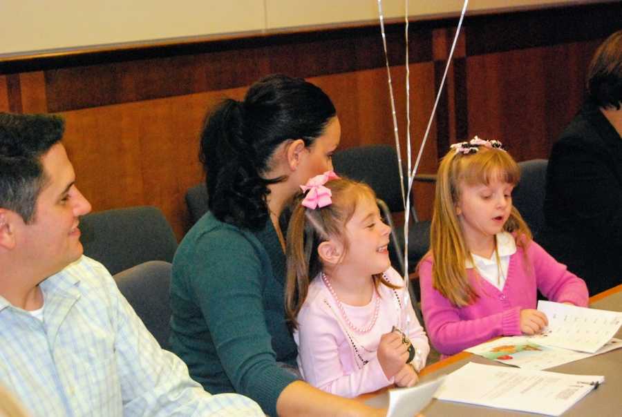 A mom sits with her daughters dressed in pink on adoption day