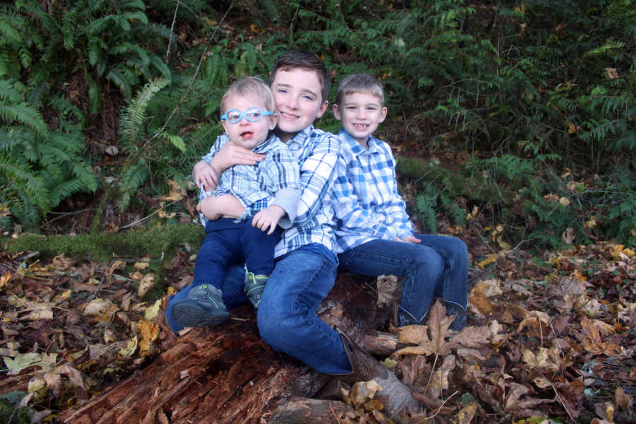 Three brothers sitting outside wearing blue shirts and smiling