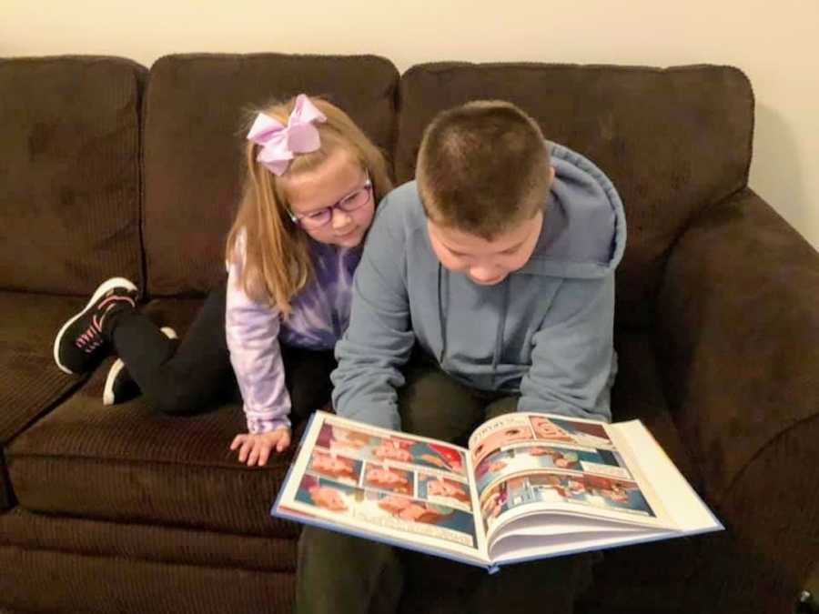 Sister and brother sitting on brown couch reading a children's book