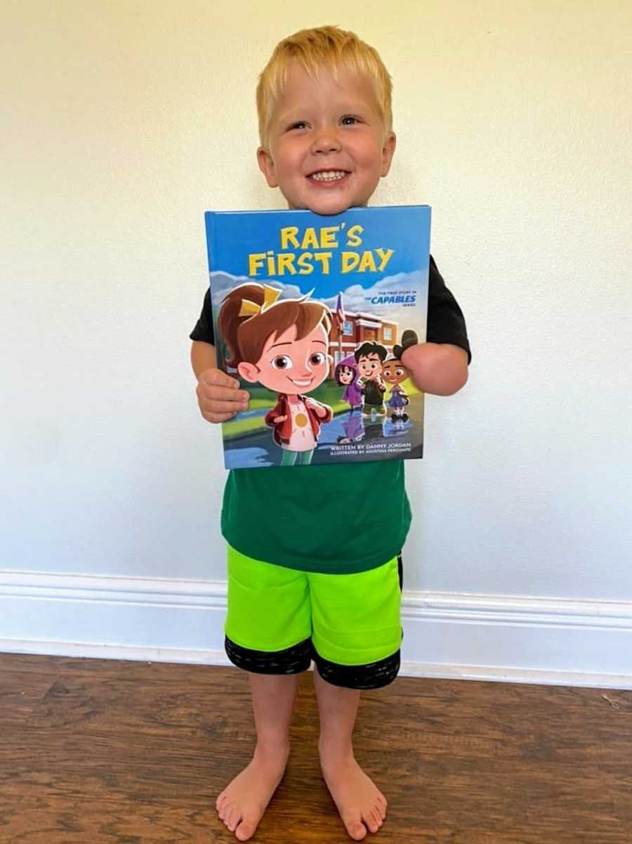 Young blonde boy with limb difference holding children's book