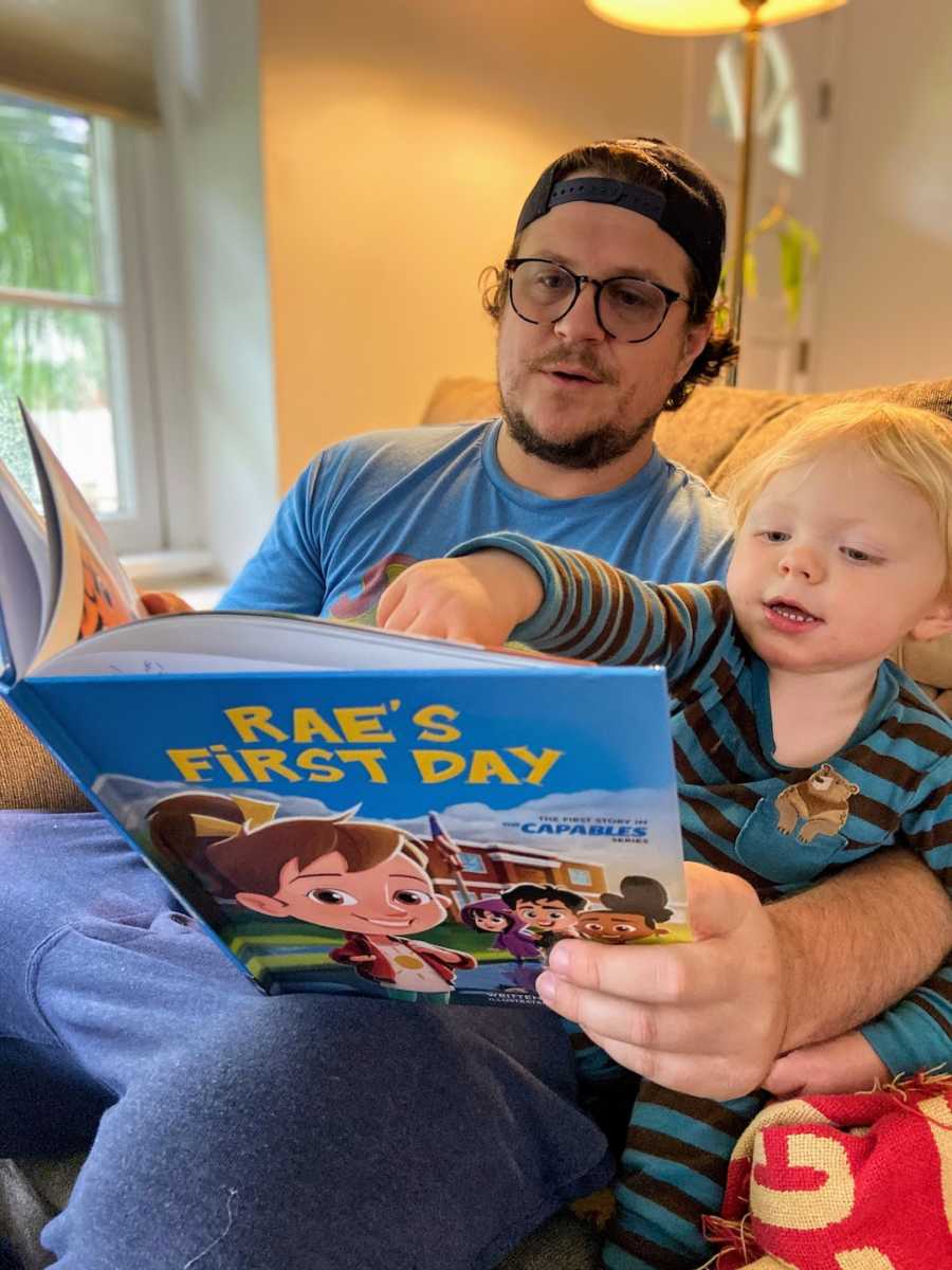 Father and son sitting on a couch reading a children's book