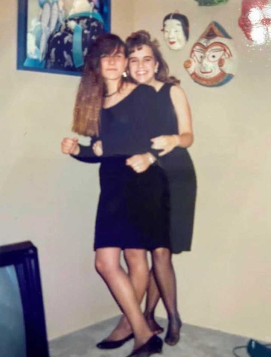A pair of friends stand together in black dresses