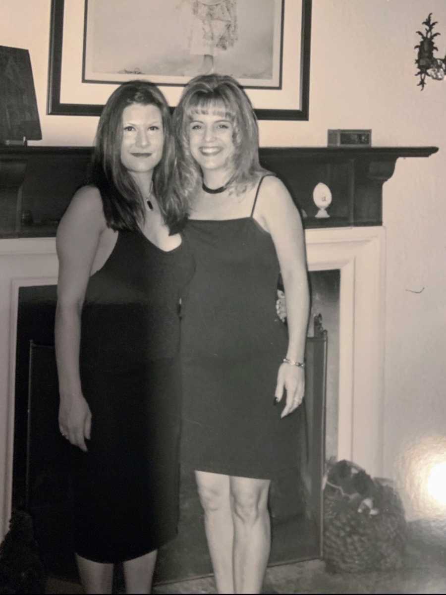 A woman and her friend stand in front of a fireplace