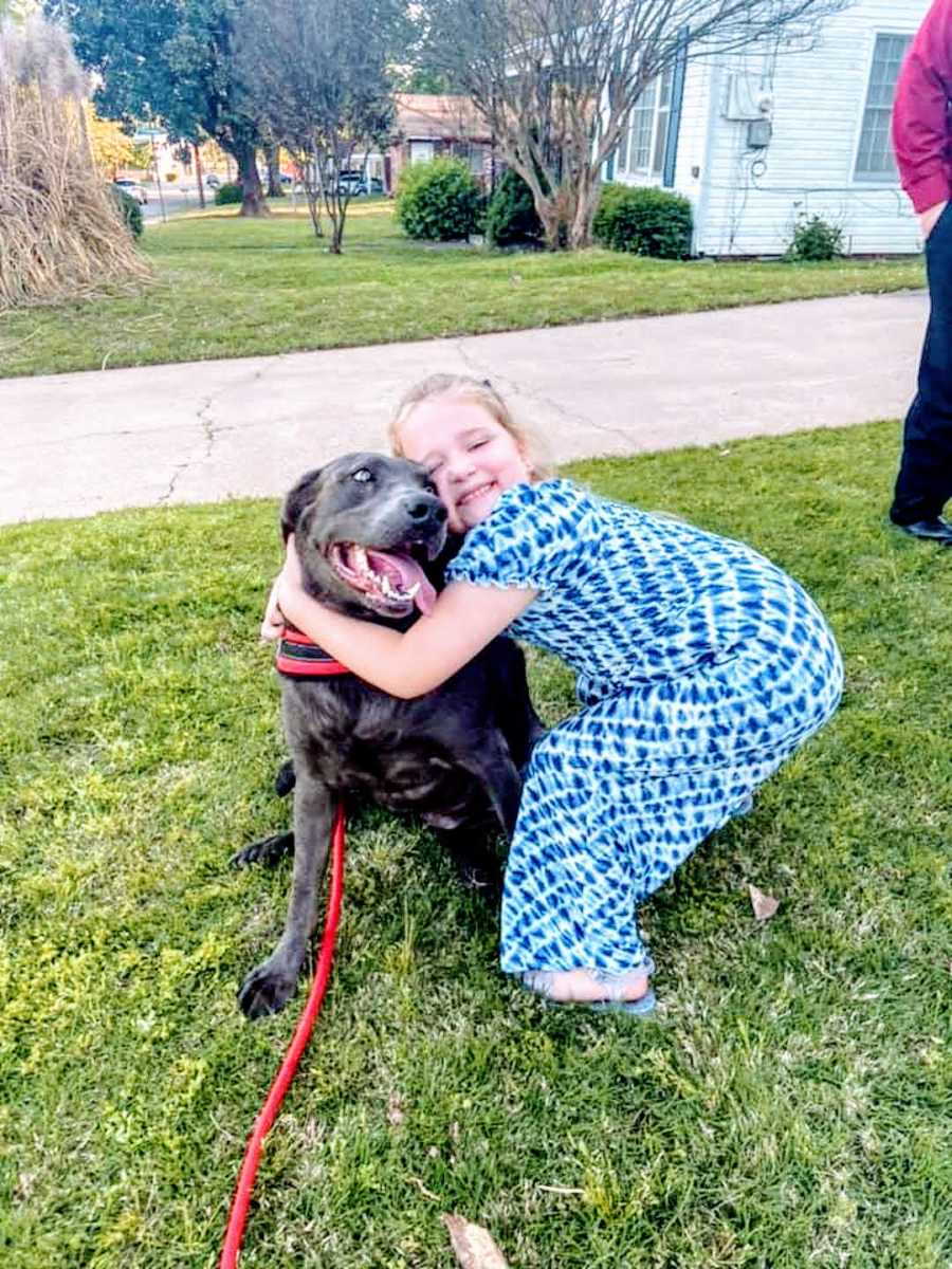 girl in blue dress hugs drooling pitbull