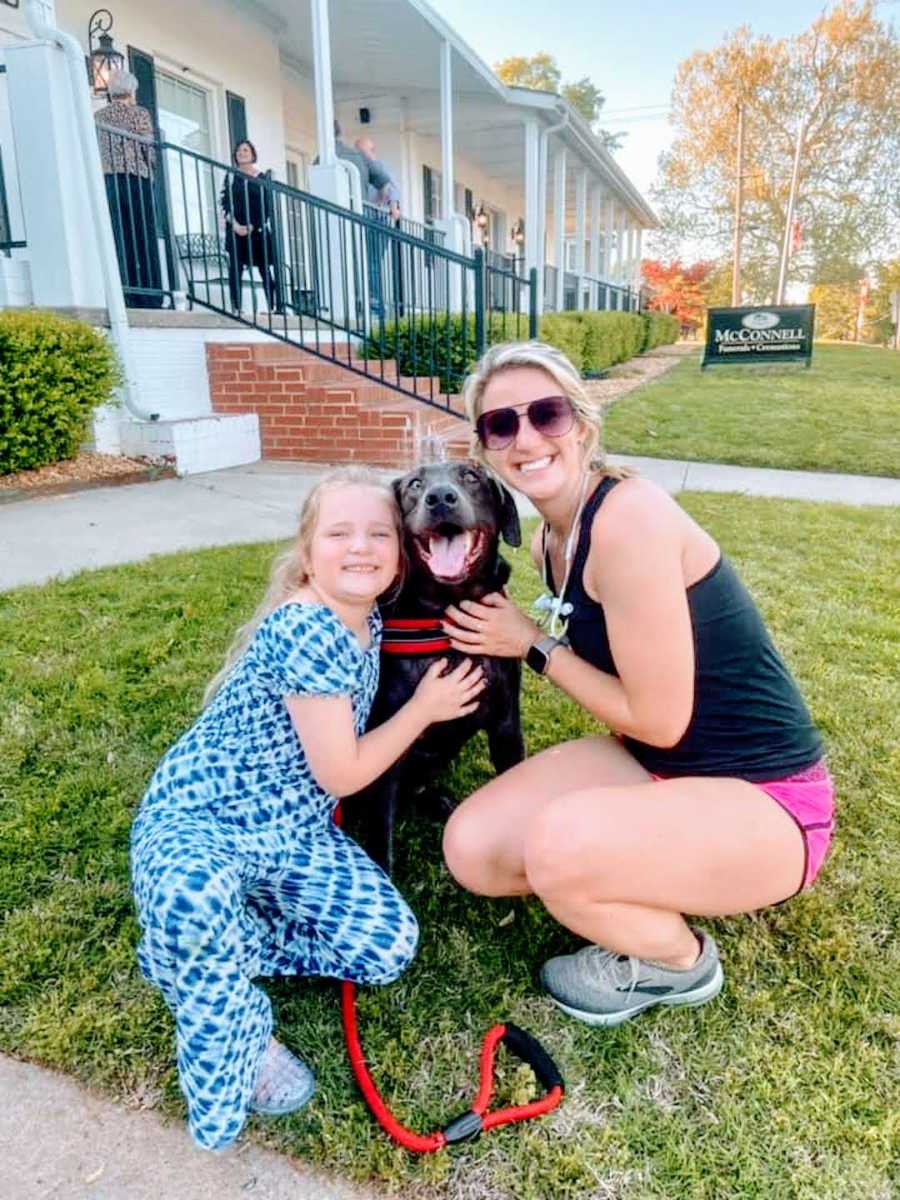 stranger in sunglasses and girl in blue dress hug pitbull outside funeral home