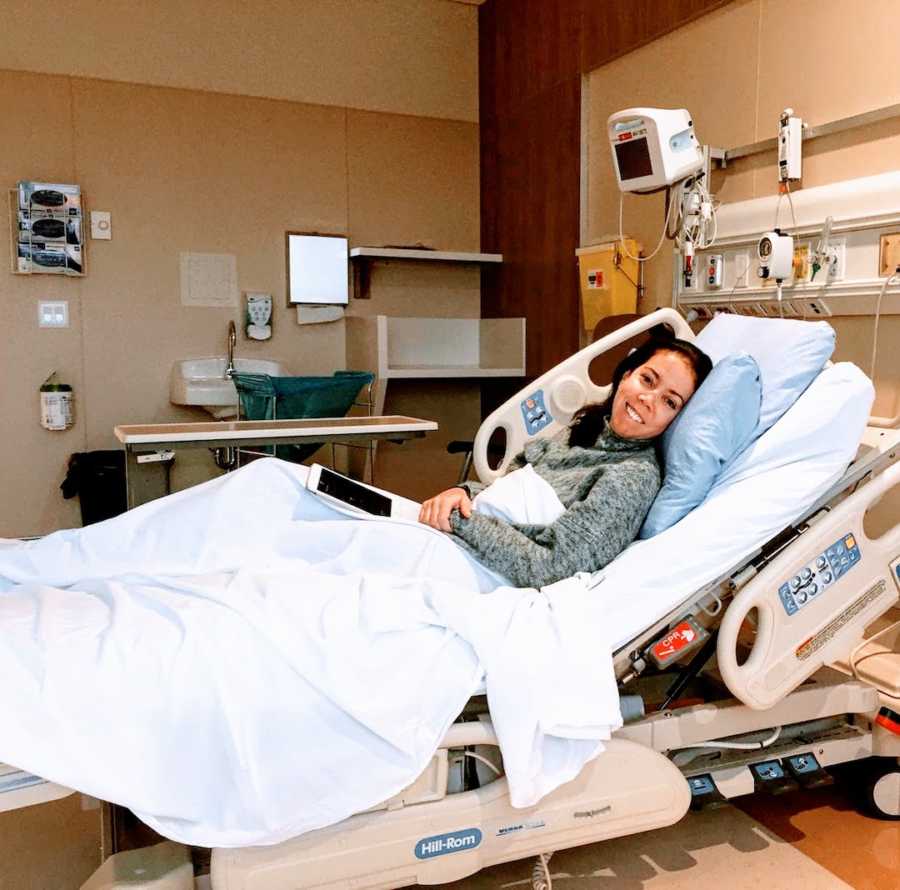 Woman smiling and lying in hospital bed with blue sheets