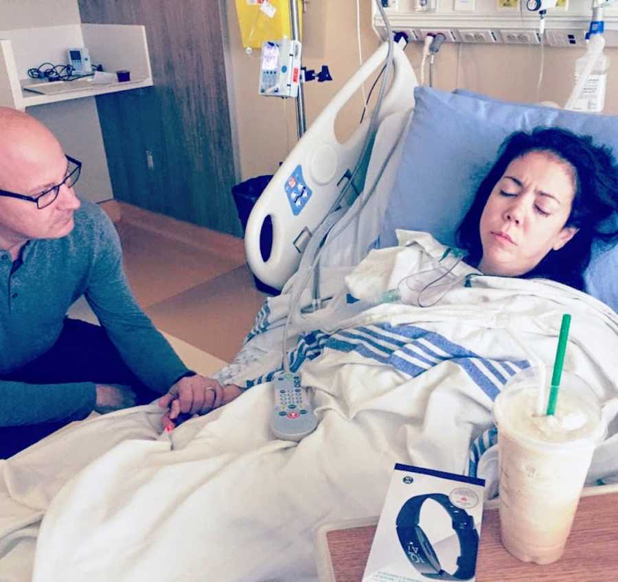 Woman sleeping in hospital bed with man holding her hand