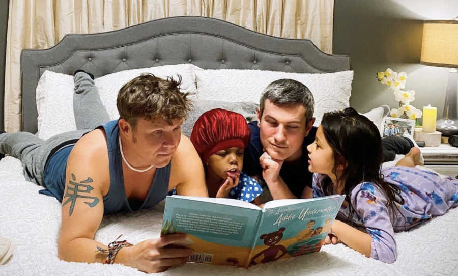 Two gay dads reading a book to their adopted daughters