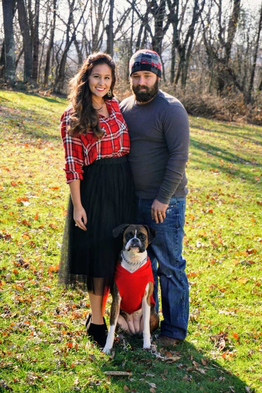 Husband and wife smiling and standing outside with Boxer dog 