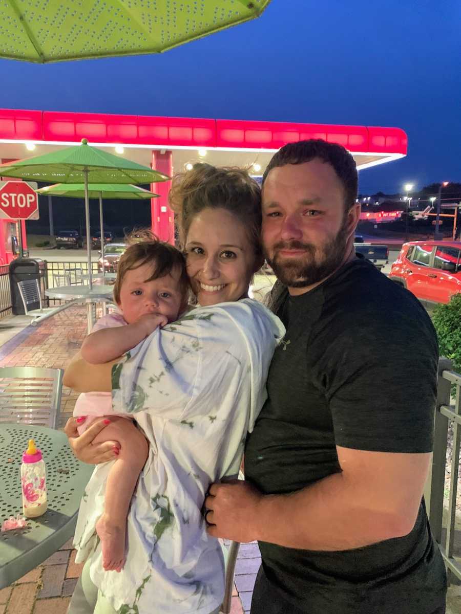 Mom and dad holding adopted daughter outside at a gas station