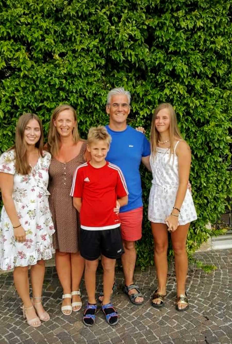 Family of five standing in front of hedge and smiling