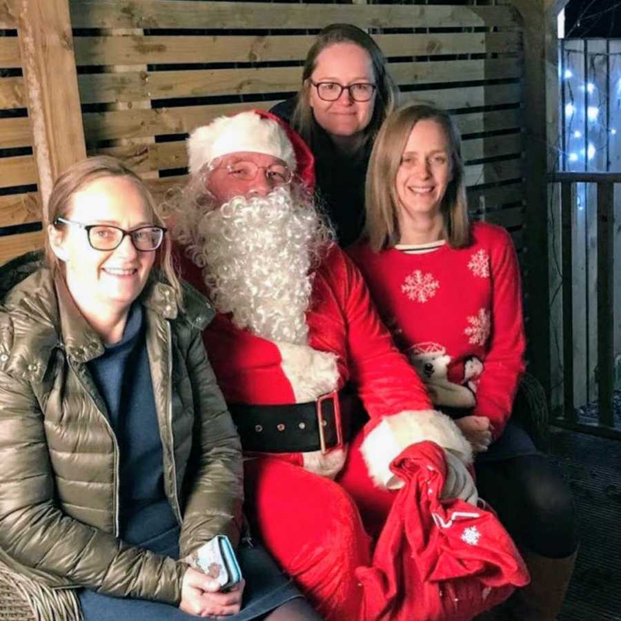 Three sisters sitting on a bench wearing red with Santa Claus