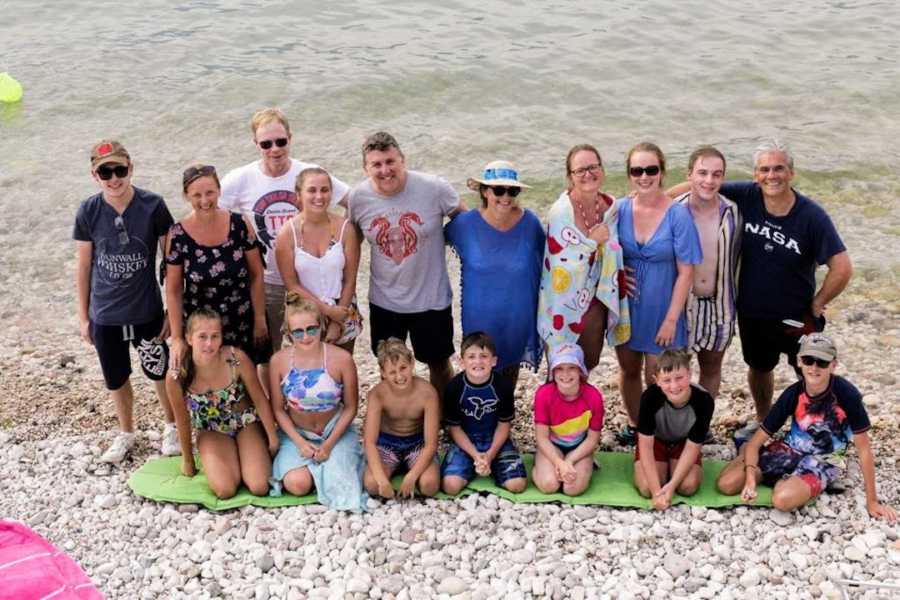 Large family standing on beach in front of water with arms around each other